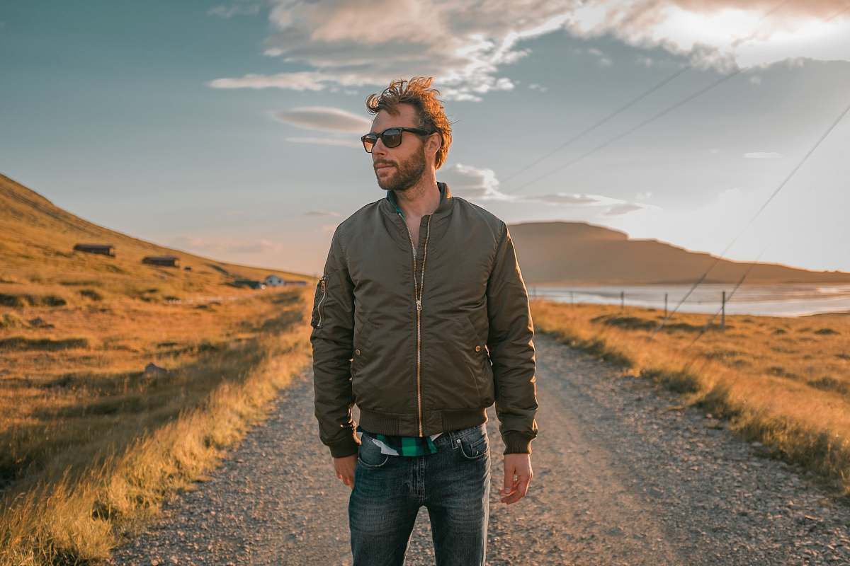 human man wearing bomber jacket standing in front of pathway people