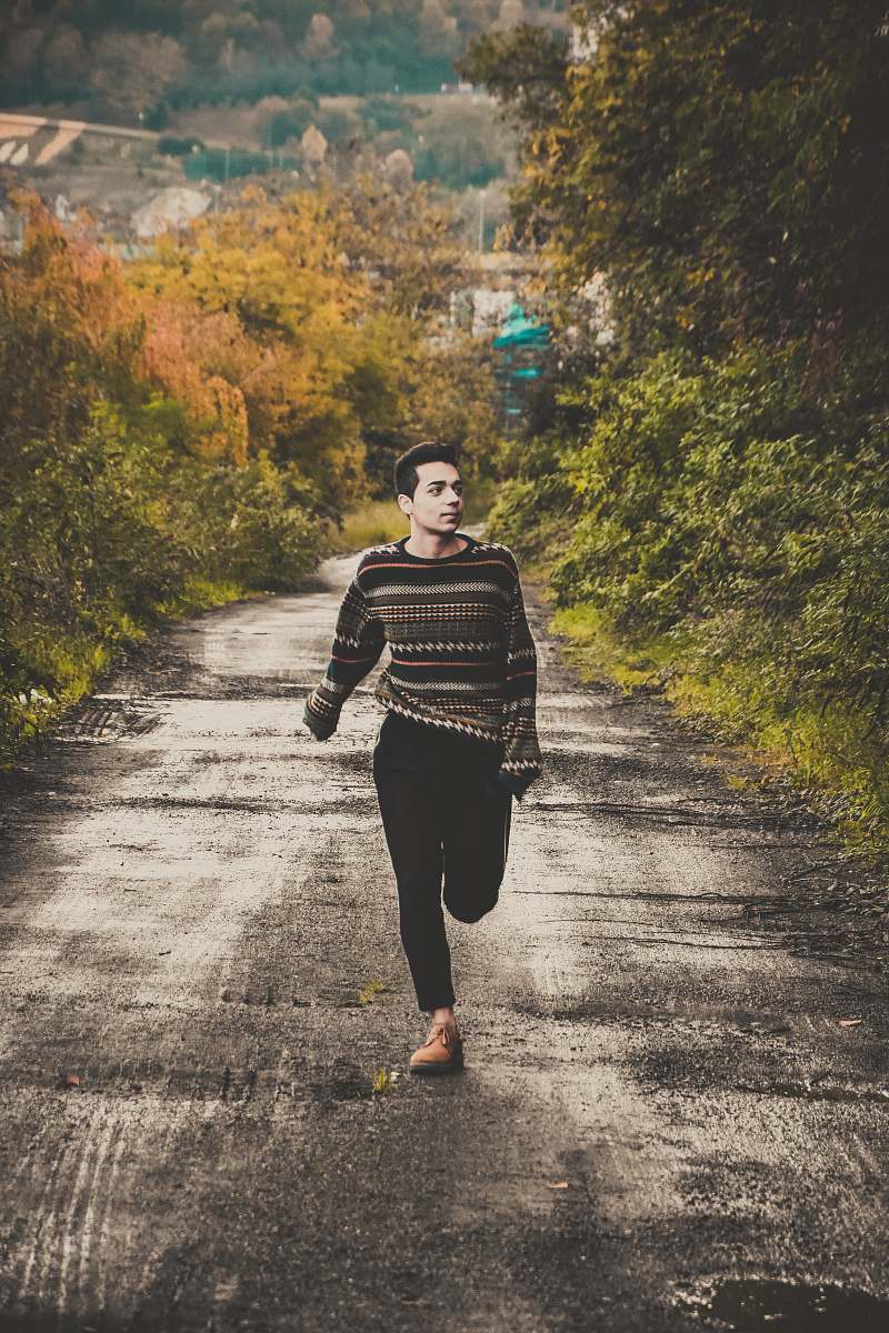 human man wearing sweater running on road between trees during daytime people