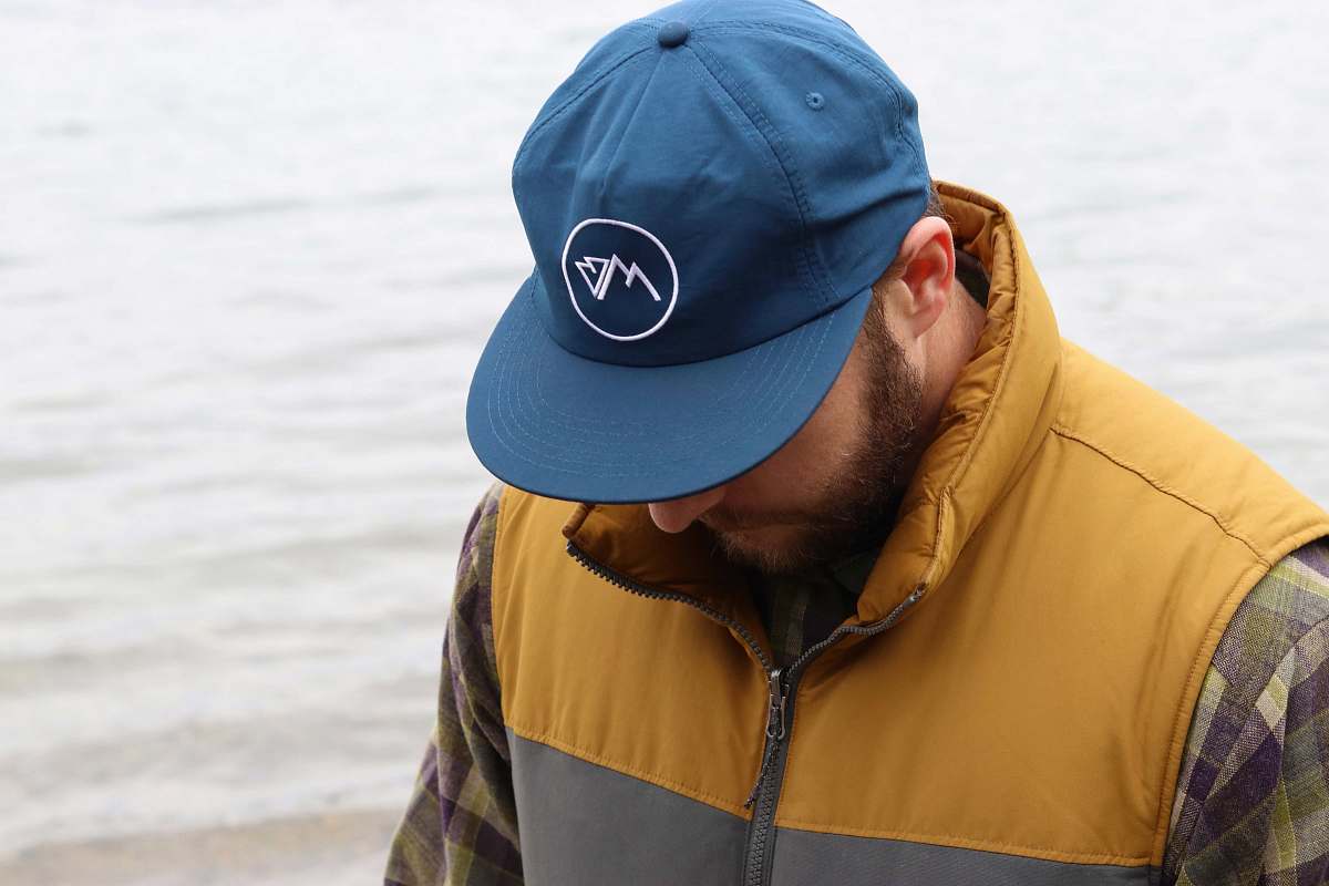 people man wearing vest and cap looking down beside body of water human