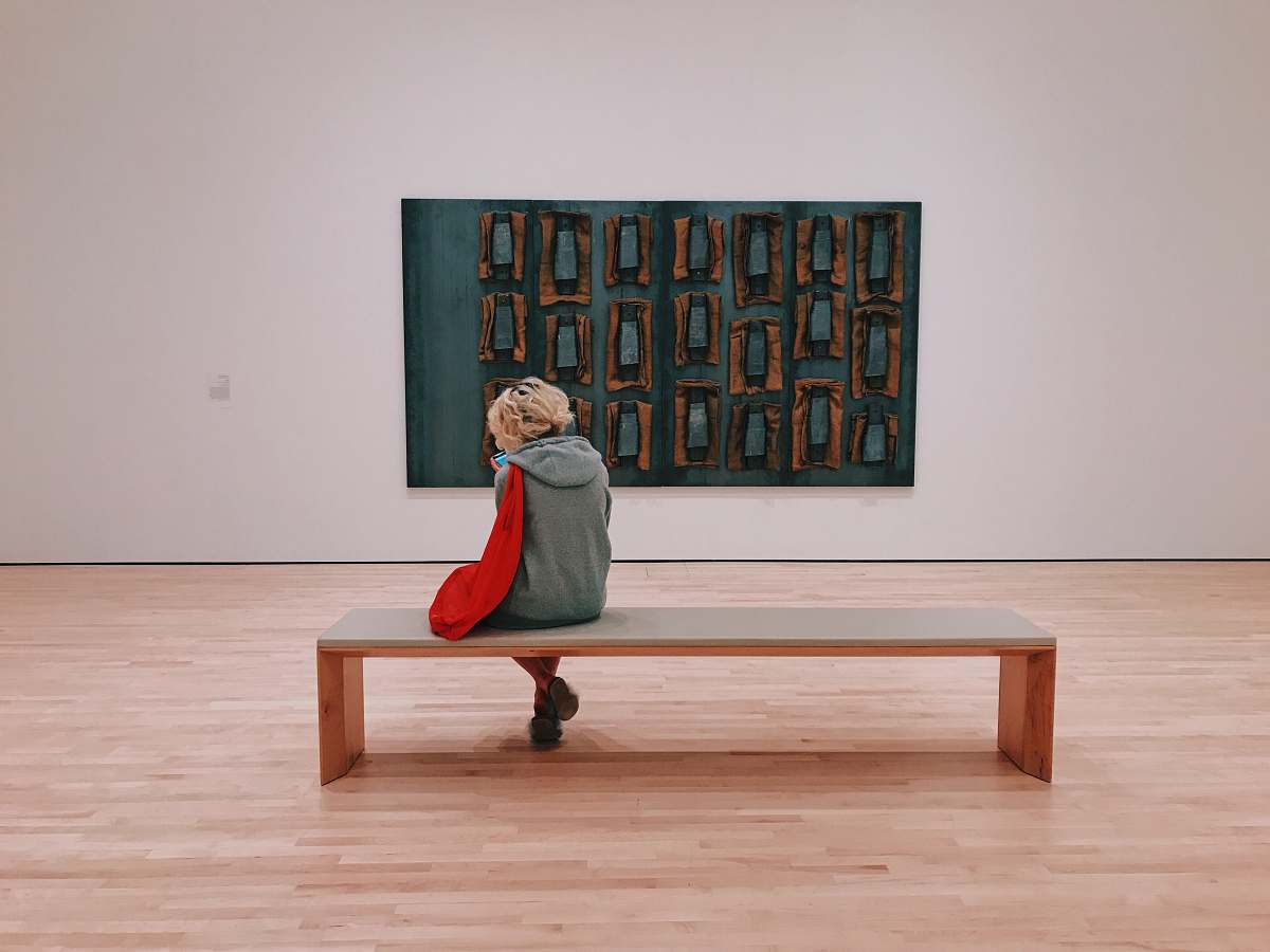 human person sitting on bench ion front of painting people