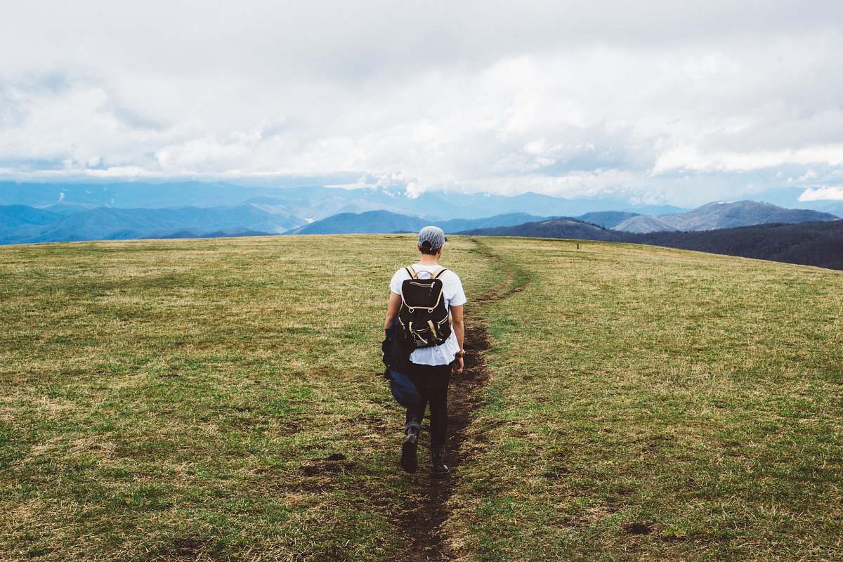 field person wearing black backpack walking on green grass field hike