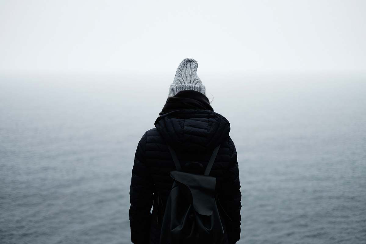 people person wearing black jacket standing in front of the ocean backpack