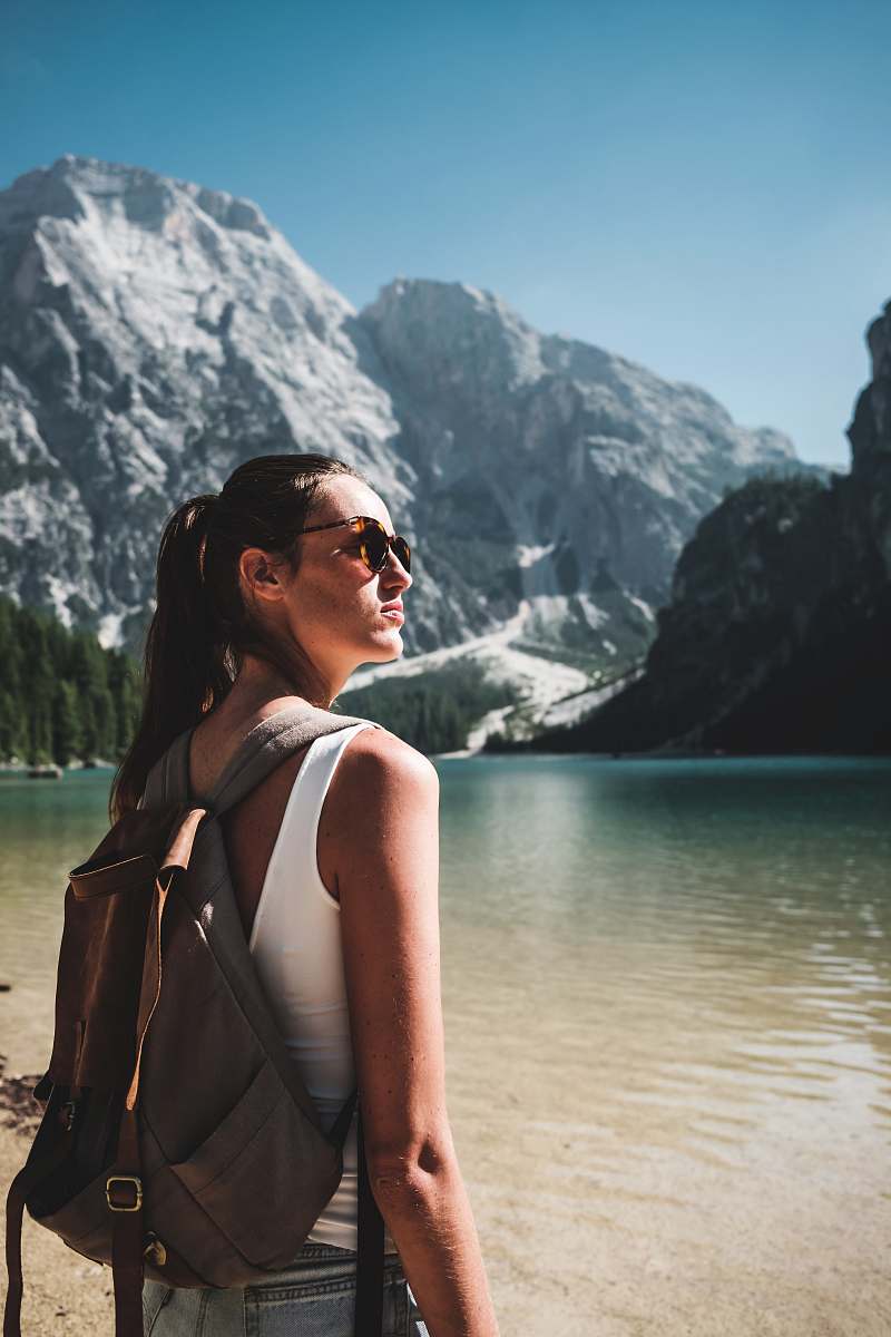 human photo of woman wearing white tank top and gray backpack standing near body of water people