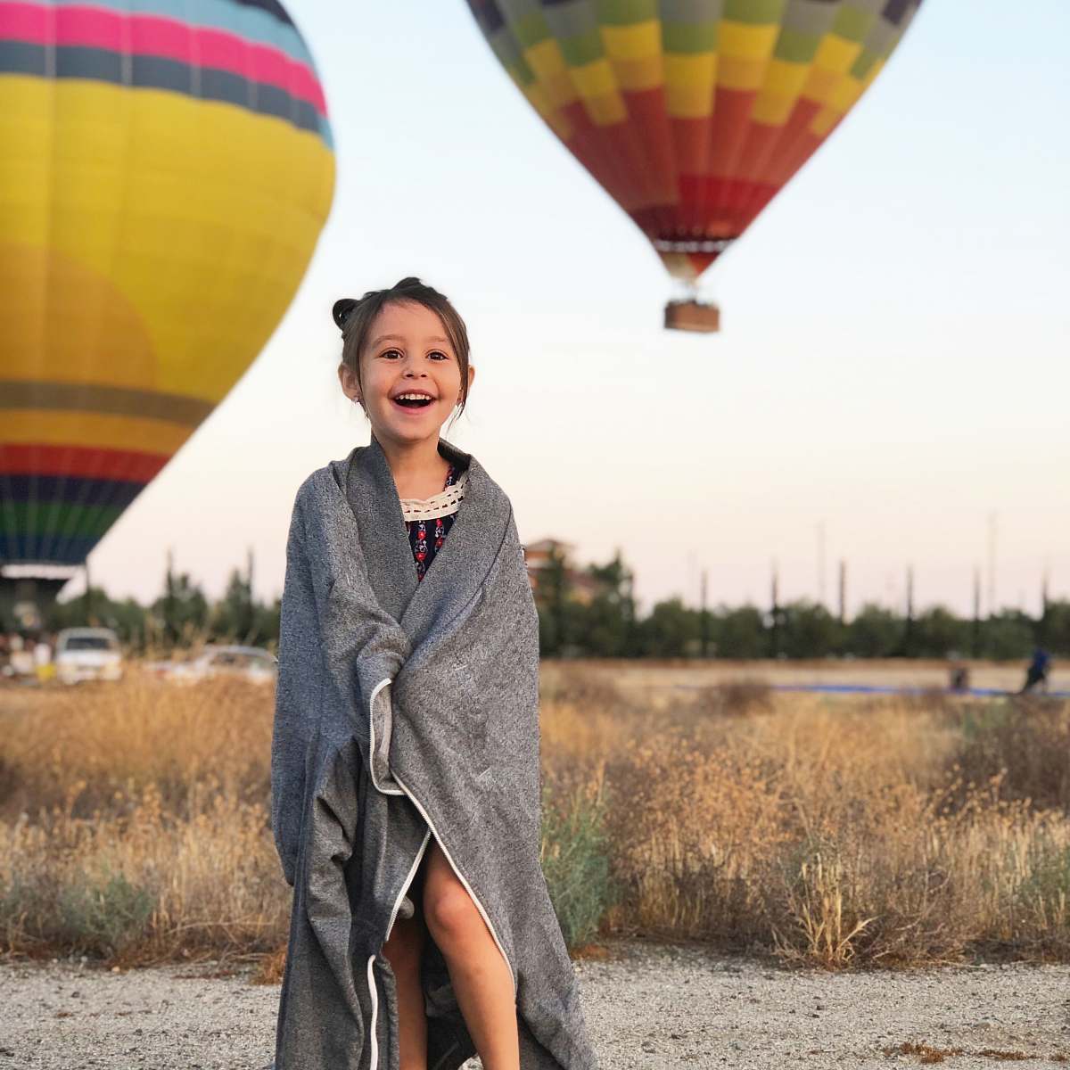 people selective focus photography of girl covered by gray scarf with background of hot air balloons human