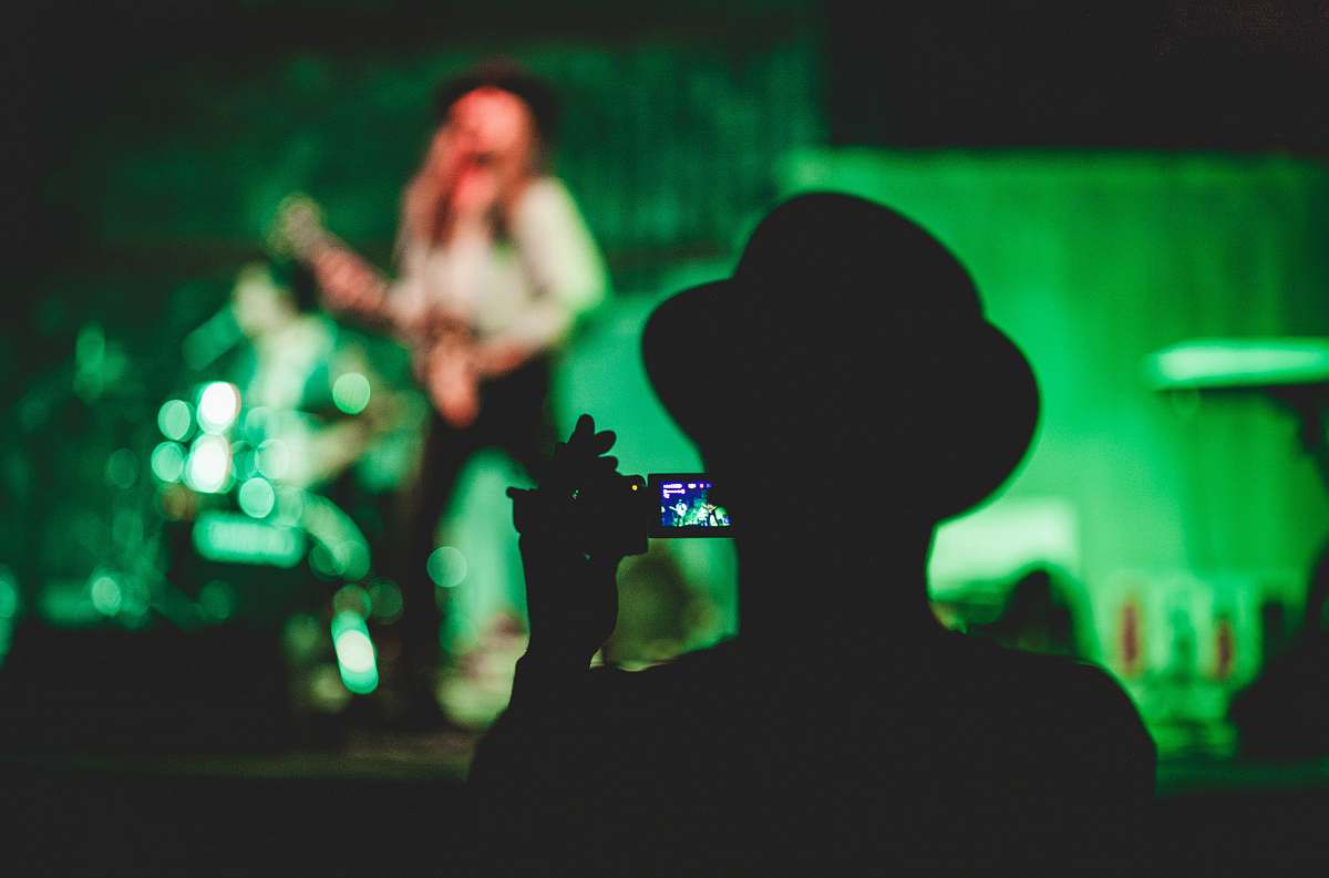 people silhouette of man holding camcorder near woman singing on stage human