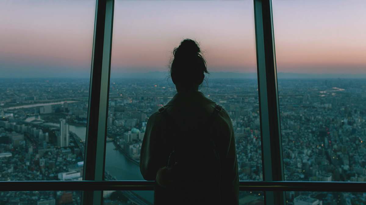 people silhouette of person standing inside the building facing the glass mirror watching the city human
