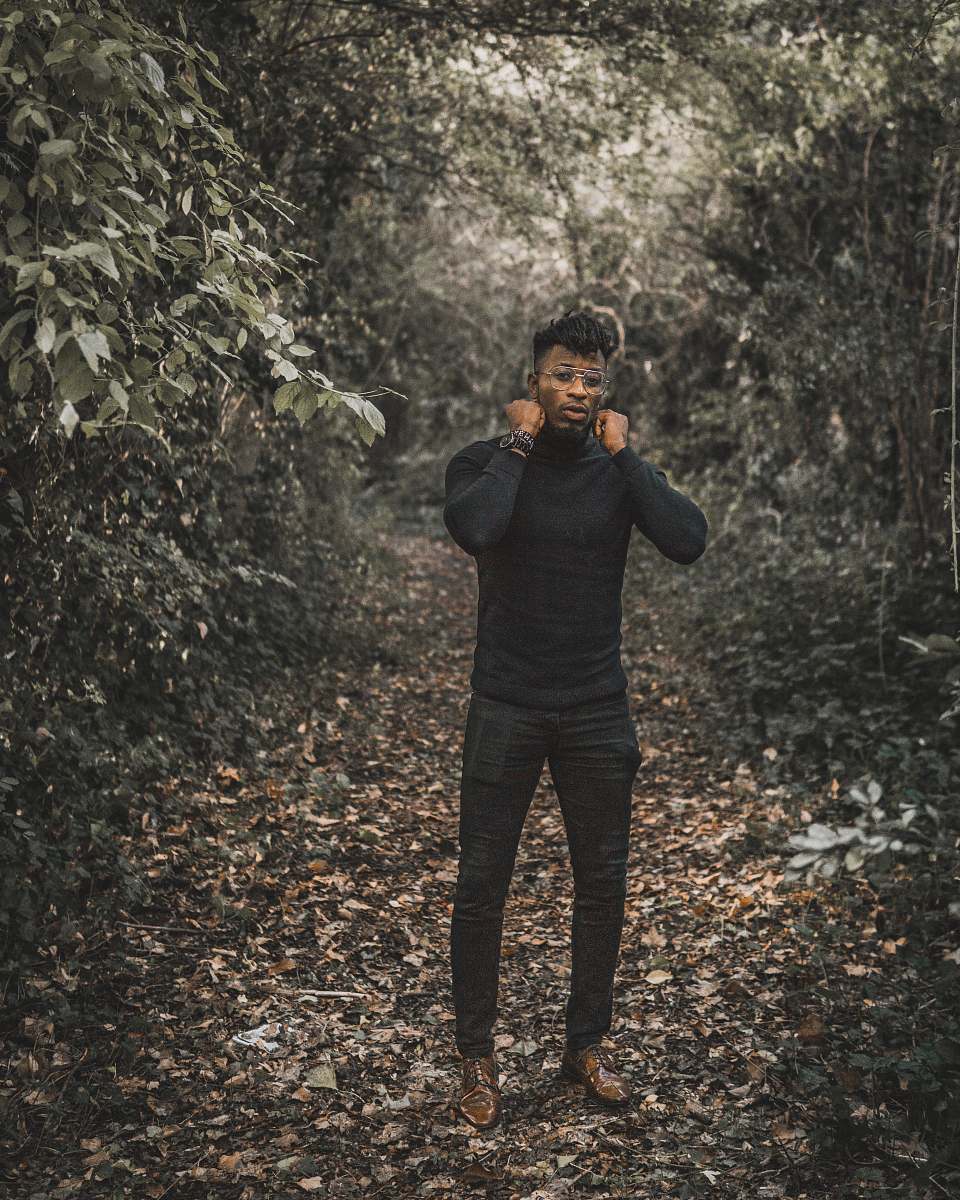 people standing man wearing black turtleneck sweater and black fitted pants surrounded with trees during daytime human