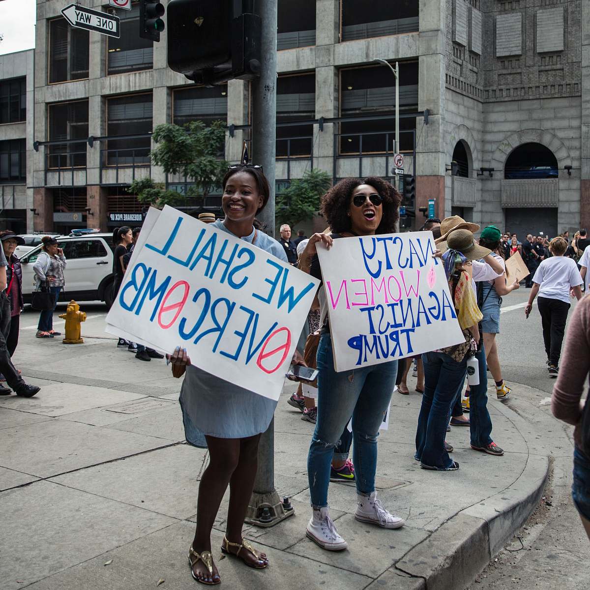 people two woman holding signage near metal post and buildings human
