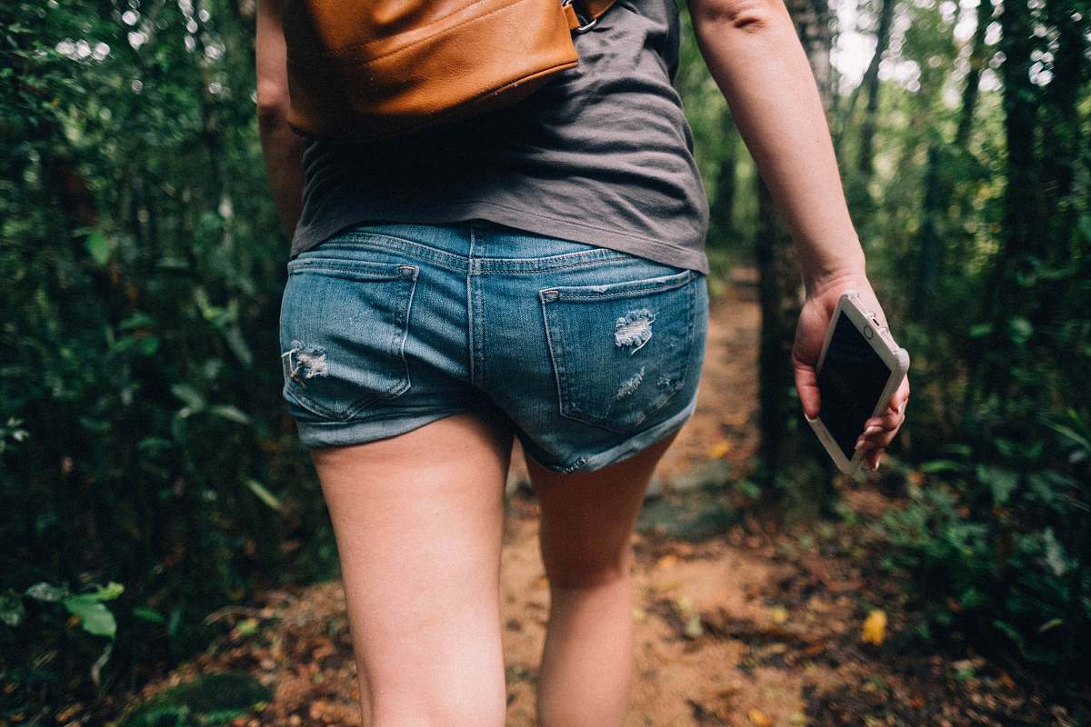 human woman holding phone walking toward trees people
