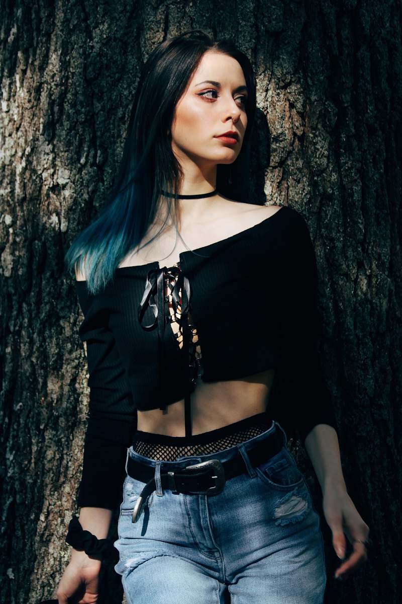 human woman in black off-shoulder top and blue denim bottoms leaning on tree trunk people