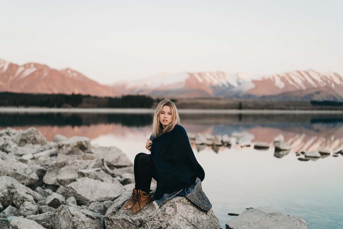 human woman in black sitting on rock near lake people