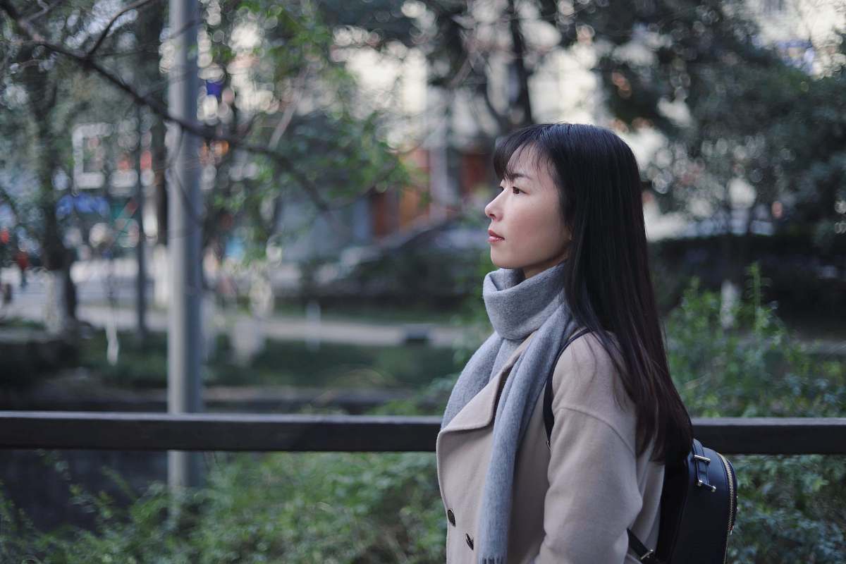 human woman in gray scarf and coat standing near bridge people