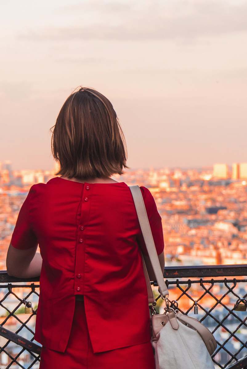people woman in red shirt and red bottoms outfit leaning on brown metal fence human