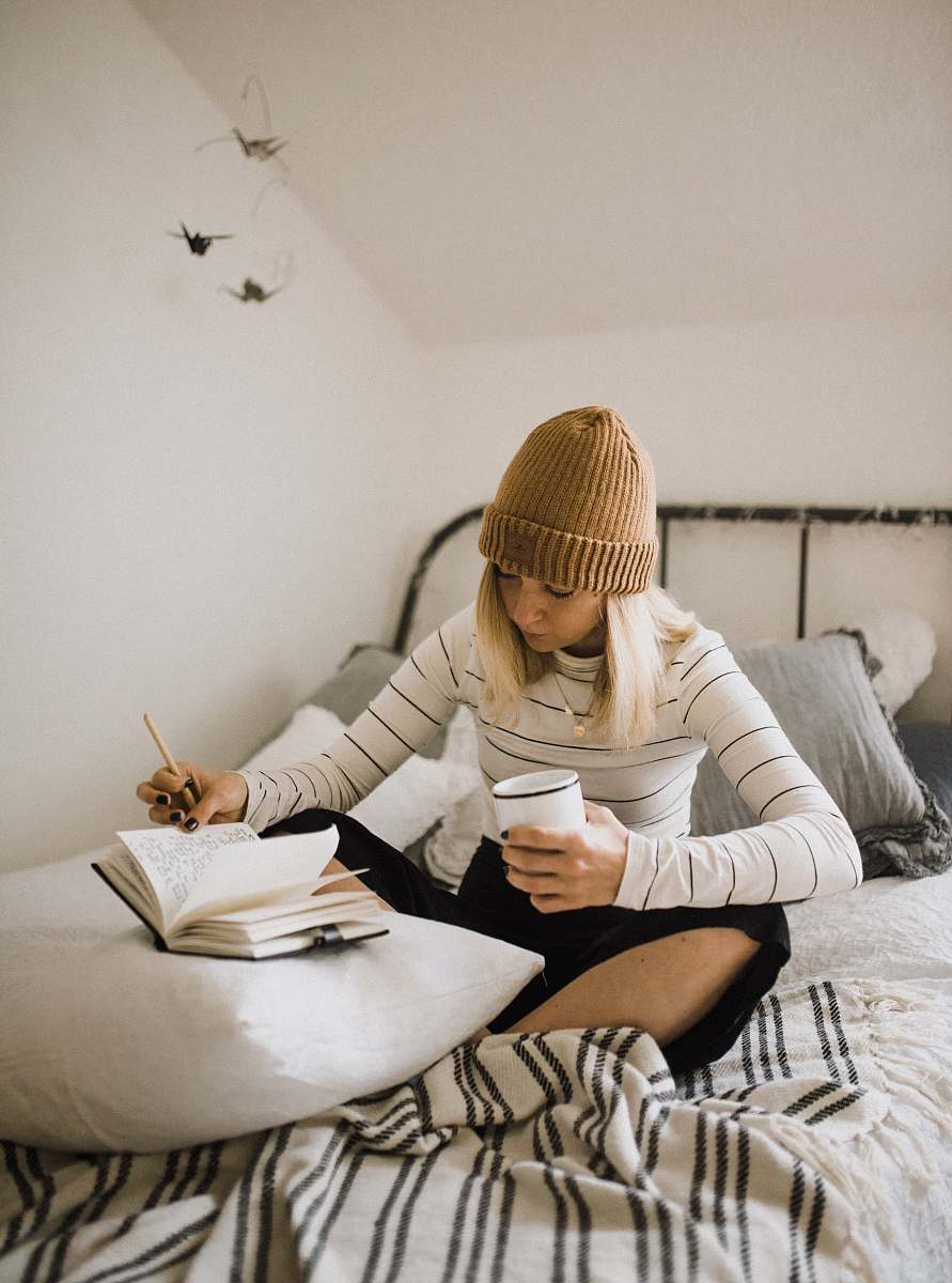 people woman in striped shirt sitting on bed while writing human