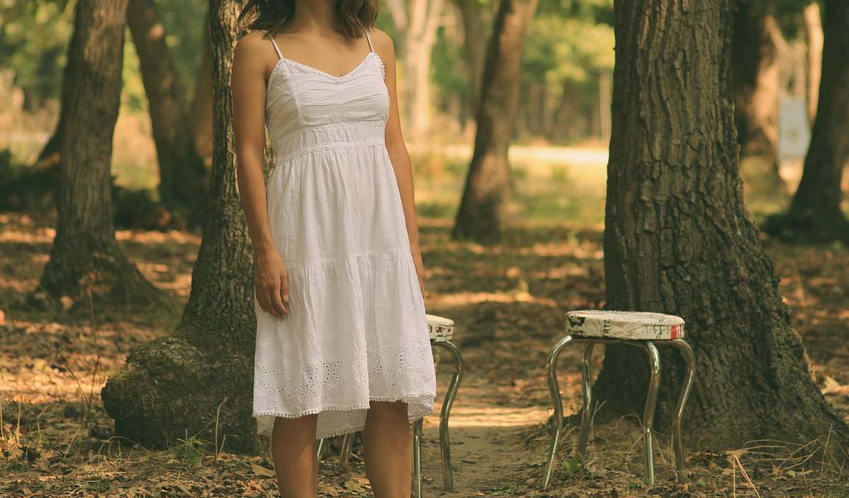 human woman in white spaghetti strap dress standing in front of white stool people