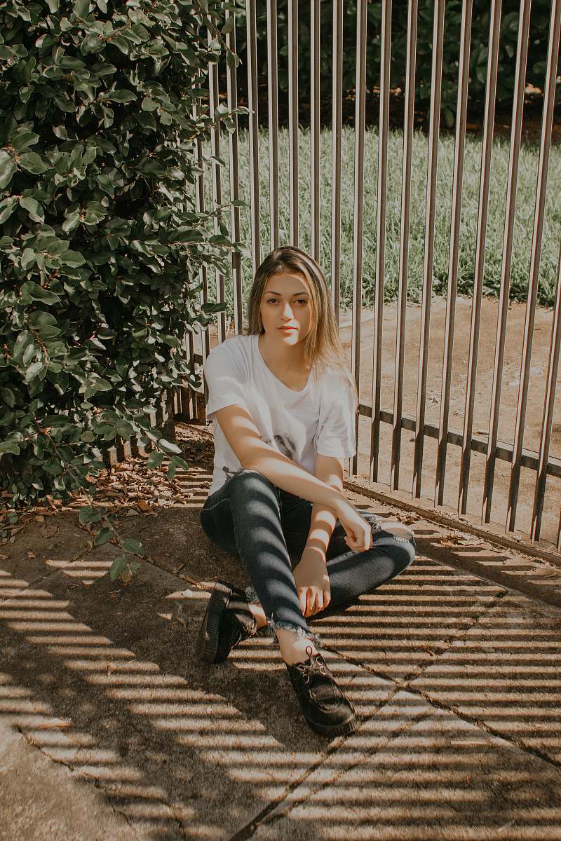 people woman sitting beside green bush and gray metal gate human