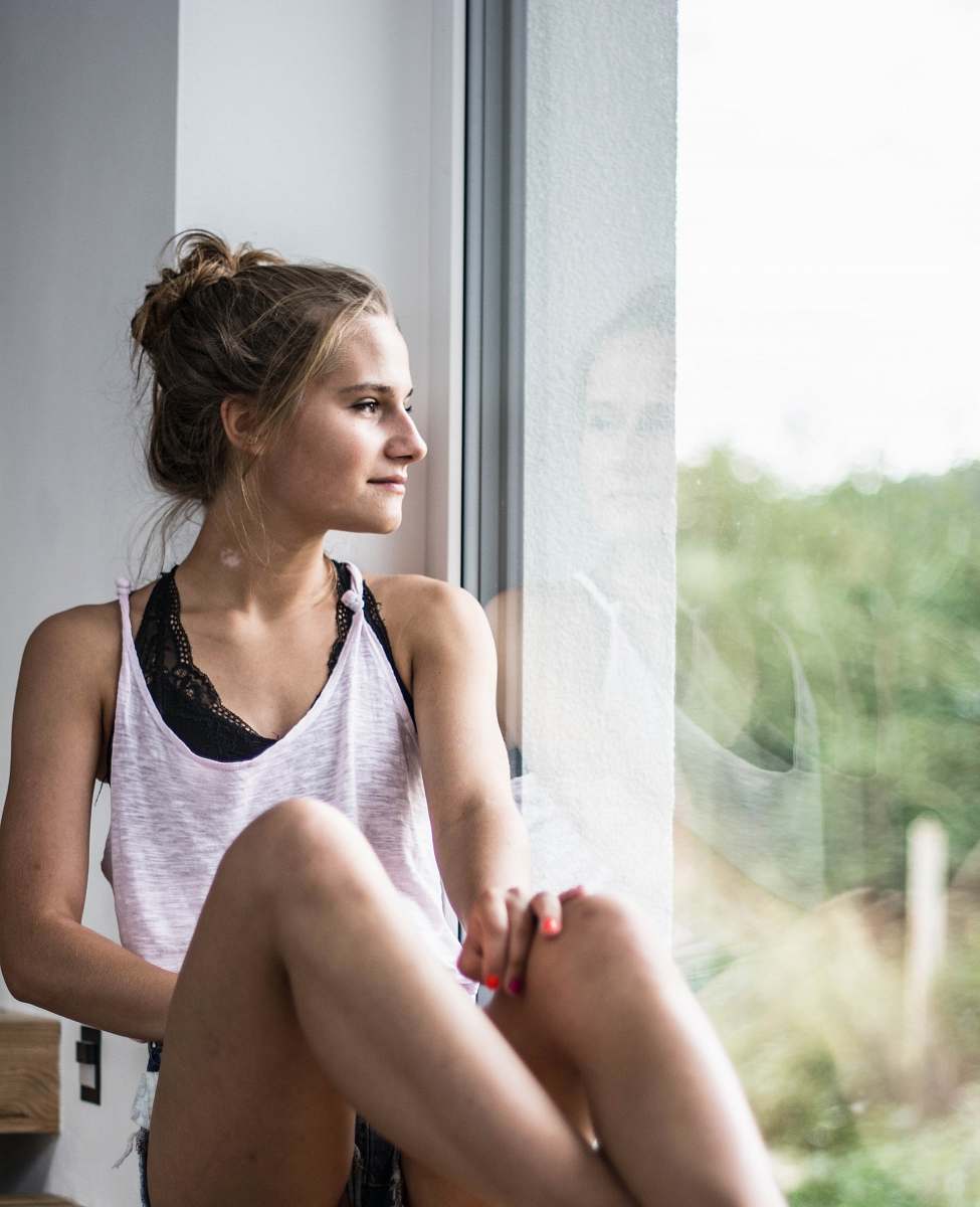 human woman sitting beside window overlooking trees people