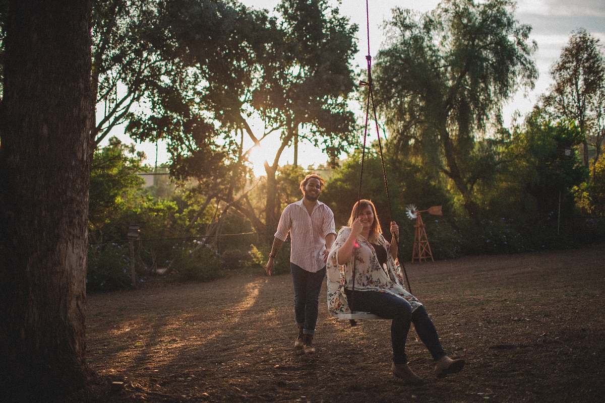 human woman sitting on swing against man standing near green trees people