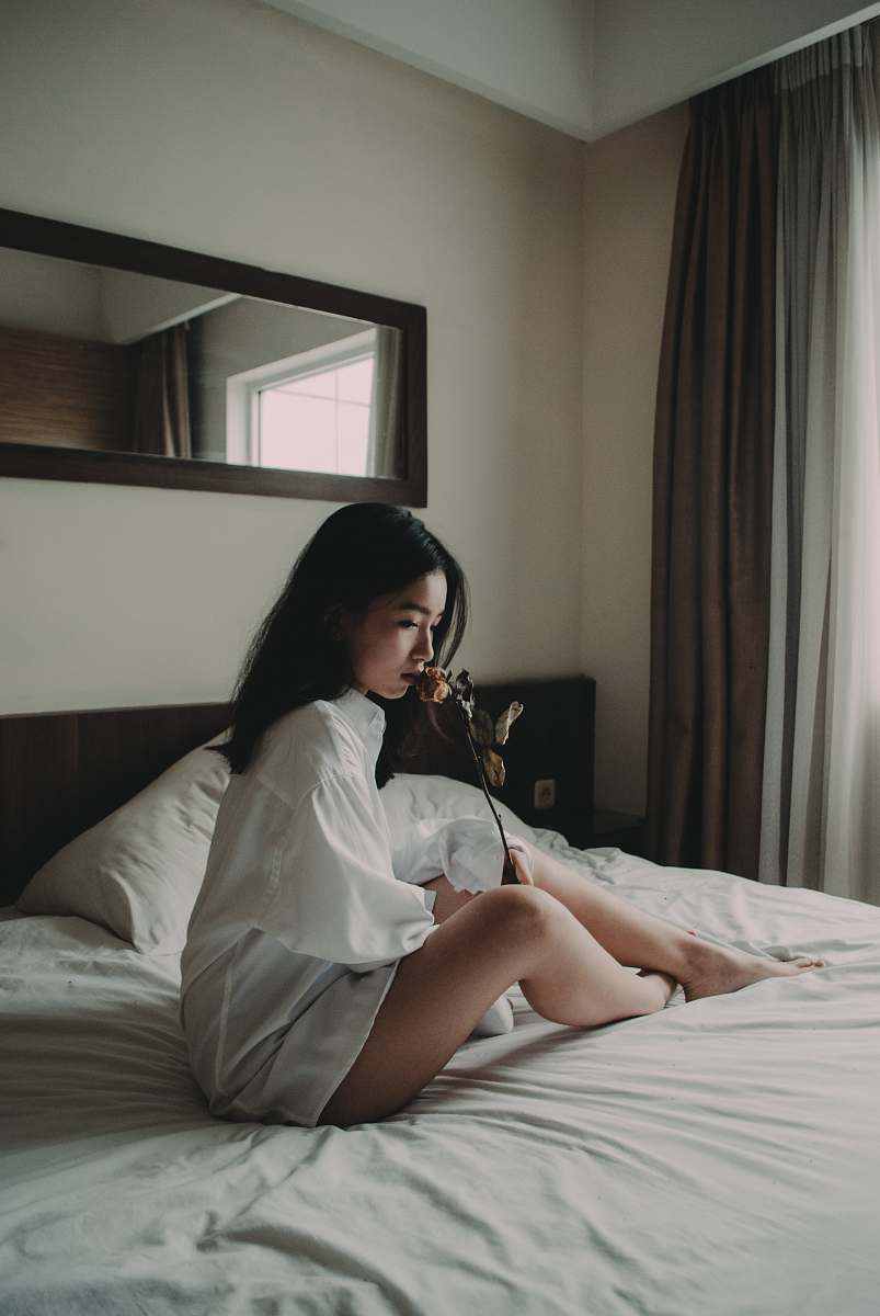 people woman sitting on white bed holding flower human