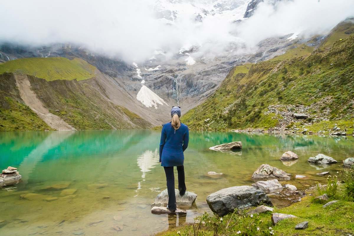 human woman standing in front of body of water and mountain people