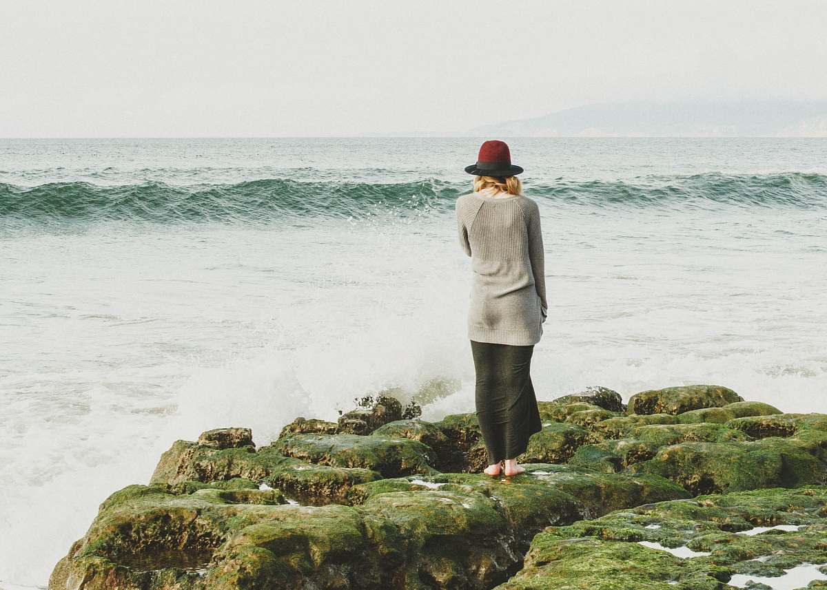 people woman standing on green rocks near body of water with waves human