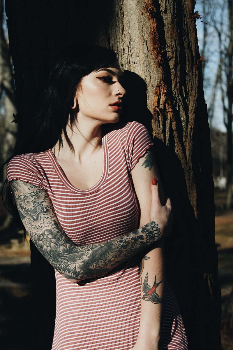 human woman with dragon tattoo on left arm standing against tree people