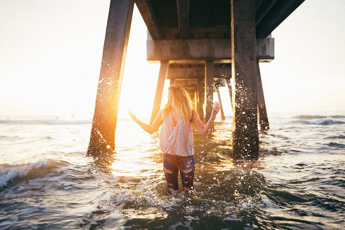 girl woman stading in water under a dock during golden time blonde