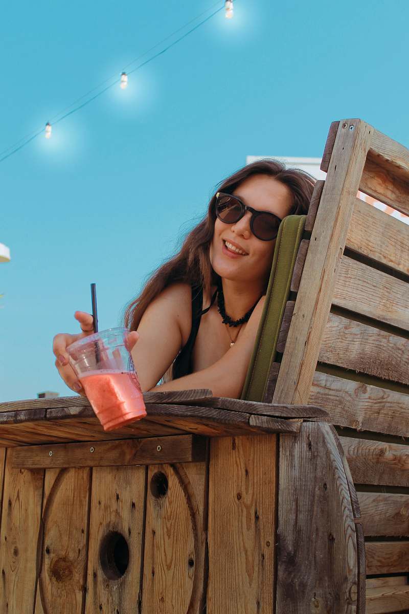 accessory woman holding disposable cup sitting on bench sunglasses