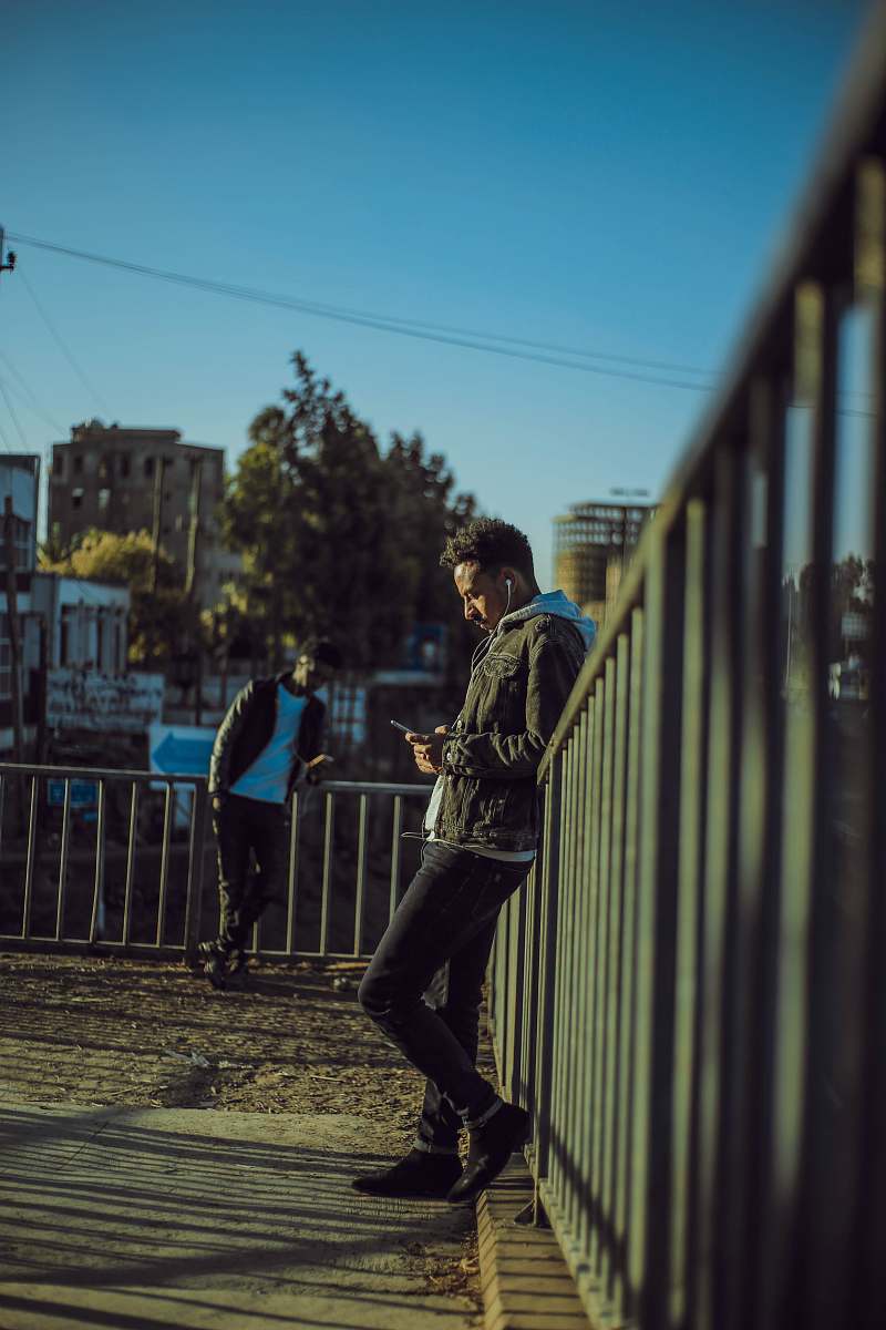 footwear man in grey denim jacket standing near metal fence shoe