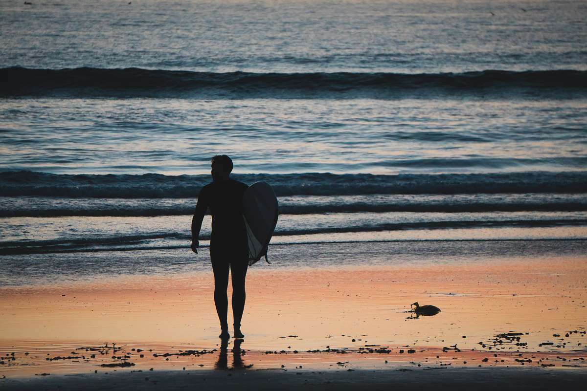 coast silhouette of man holding surfboard walking near shoreline ocean