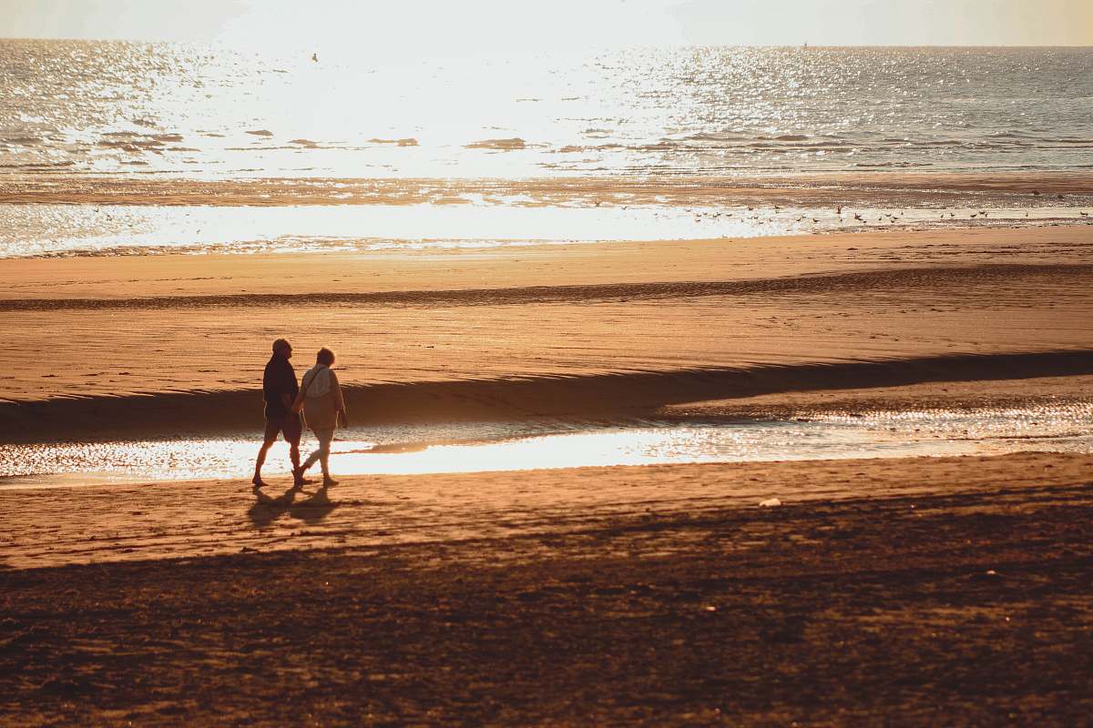 coast two person walking beside beach ocean
