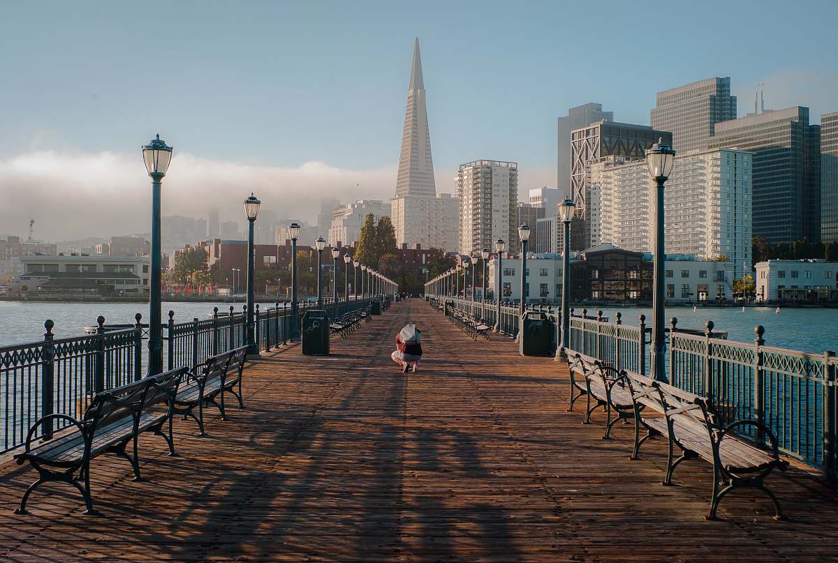 bench person on brown pathway towards building boardwalk