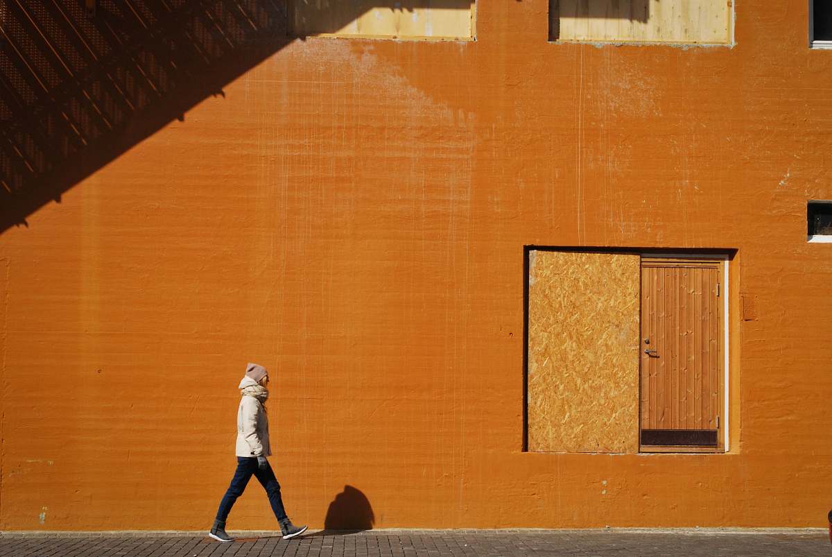 orange man walking beside orange building at daytime wall