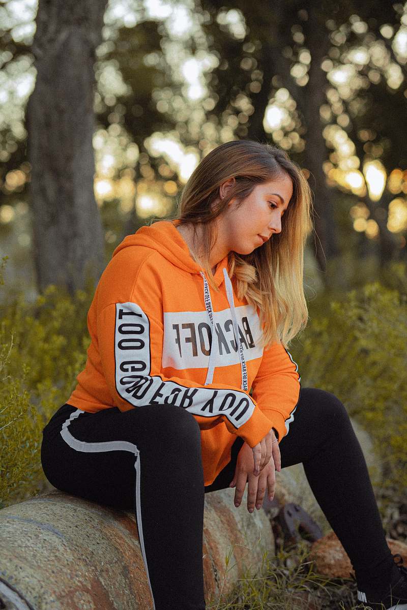 apparel woman in orange and white pullover hoodie and black leggings sitting on stone during daytim sleeve