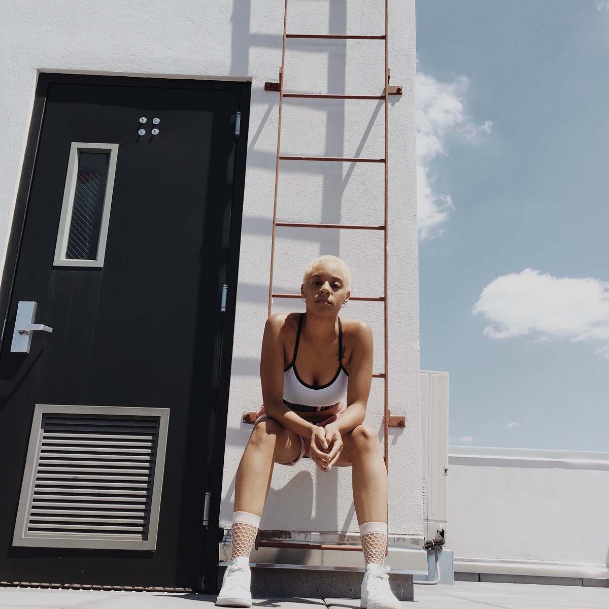 apparel woman in white and black sports bra sitting on orange metal fire ladder home decor