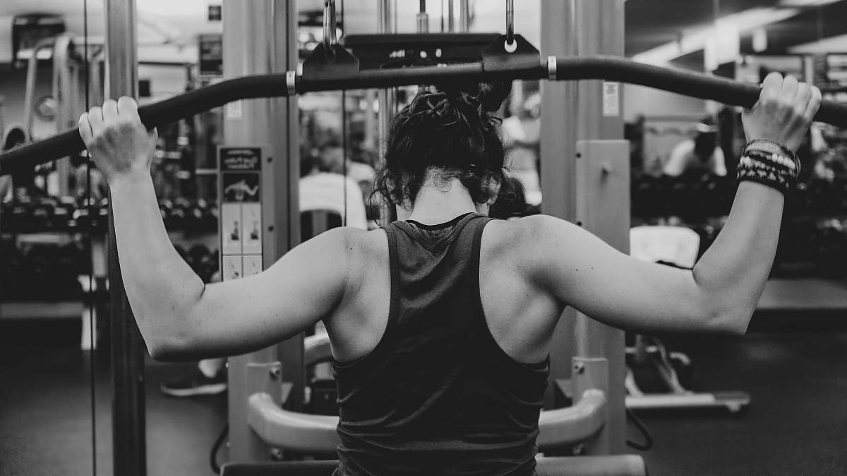 human grayscale photography of woman holding lateral pull down machine black-and-white