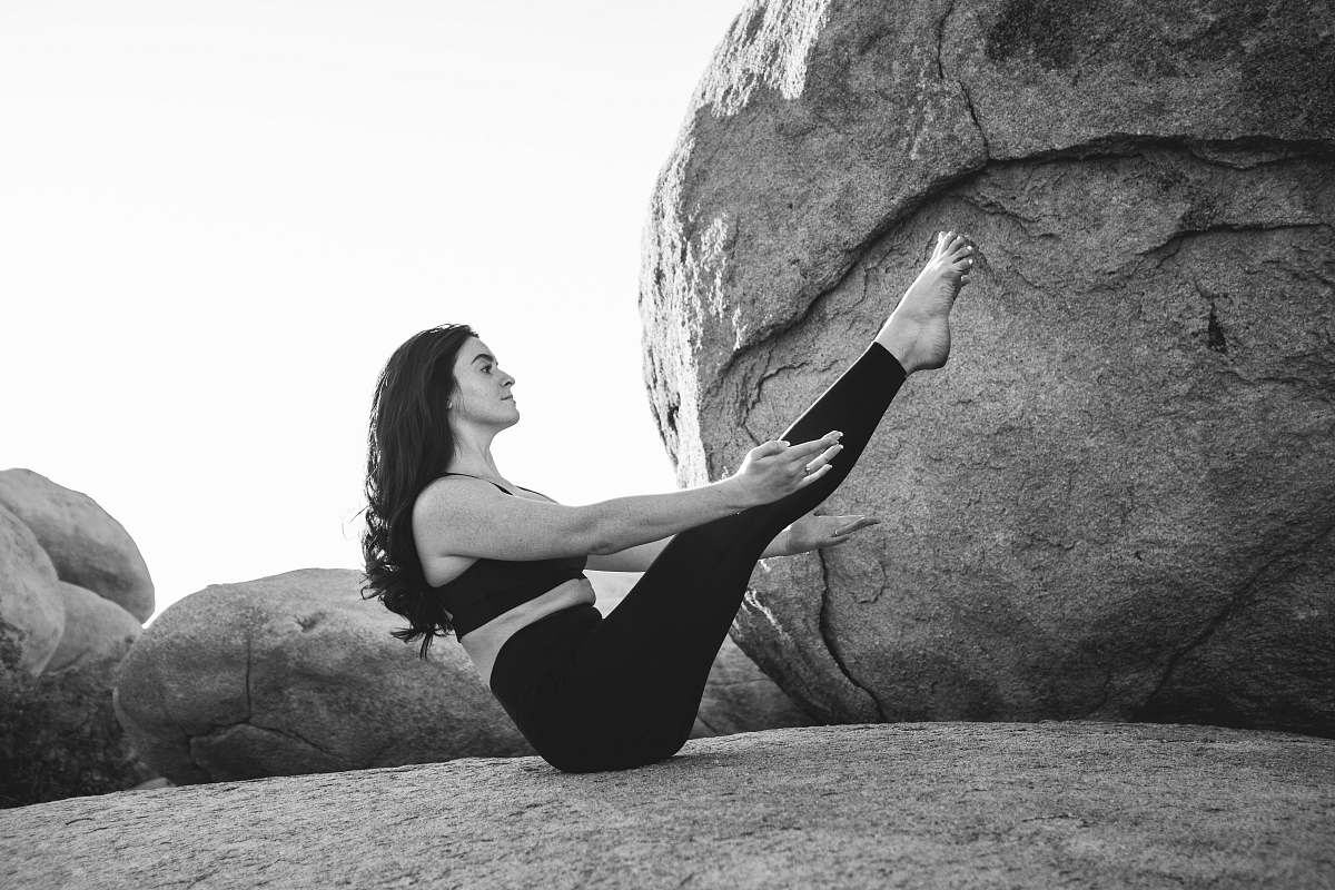 black-and-white grayscale photo of woman exercising on top of large rock rock