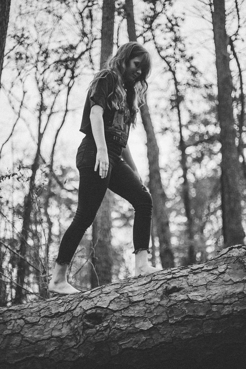 person grayscale photo of woman walking on log black-and-white