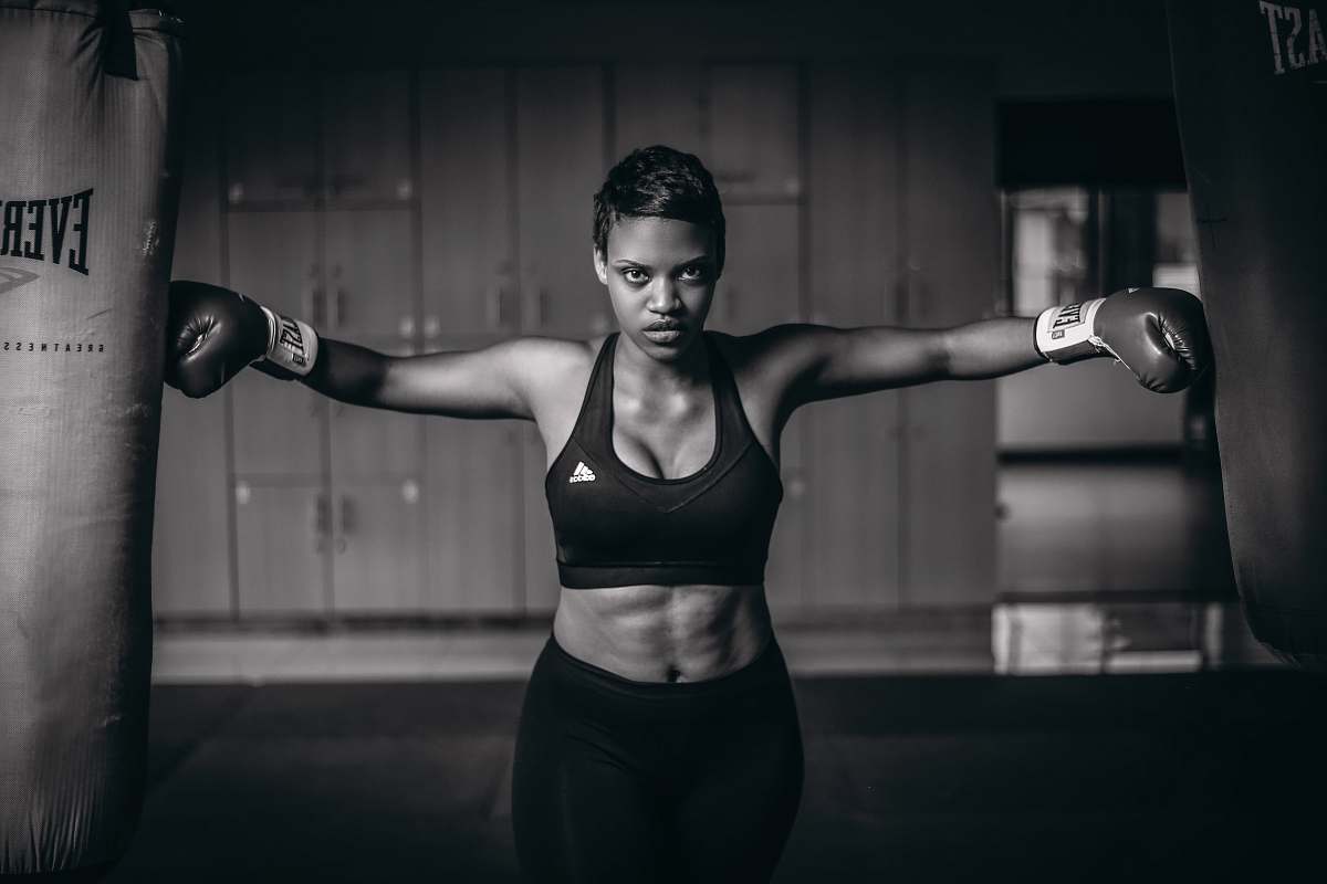 person grayscale photo of woman with gloves touching heavy bags fitness