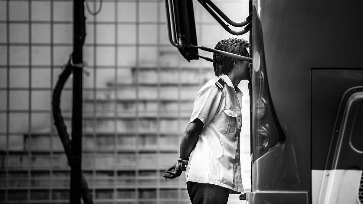 person grayscale photography of man standing beside bus black-and-white