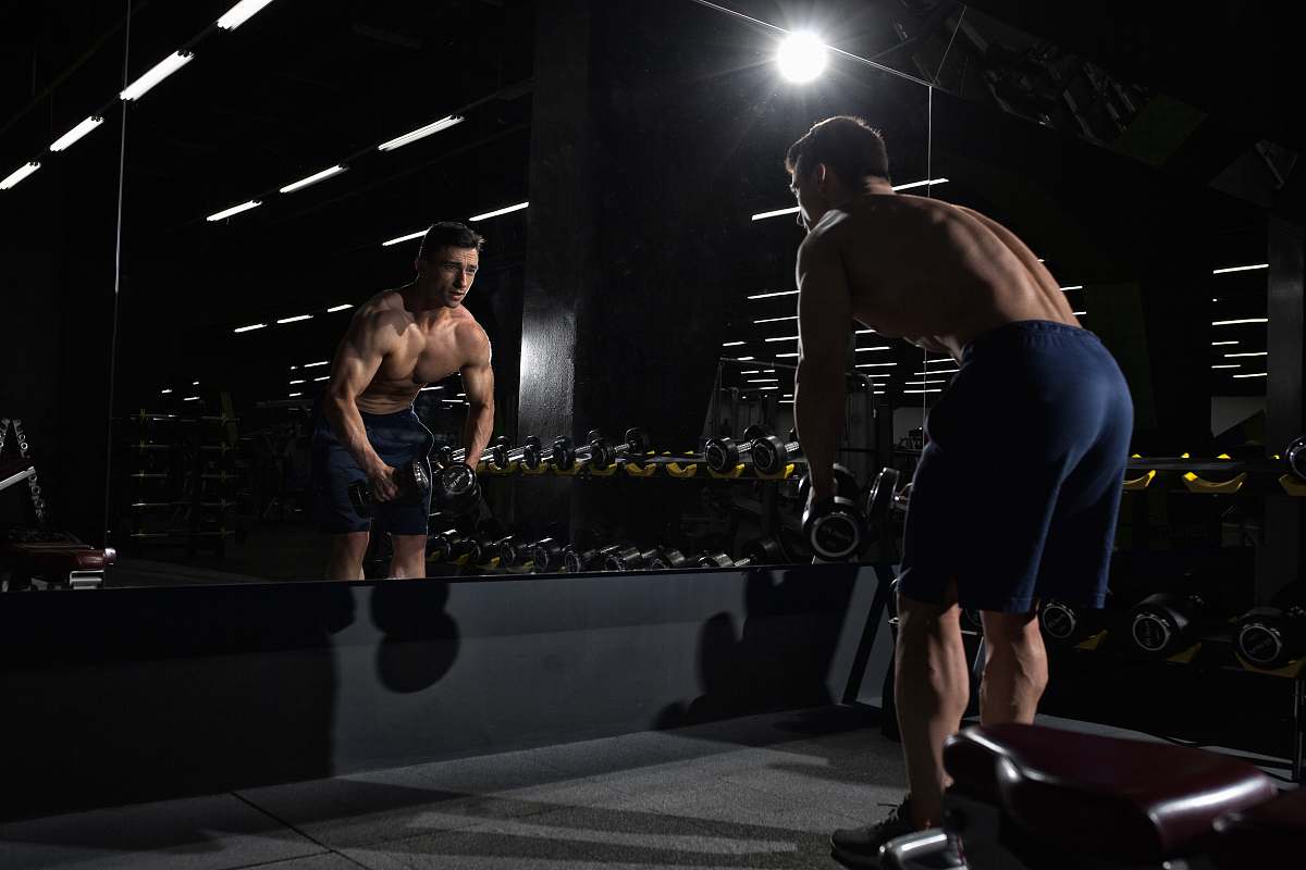 person man carrying dumbbell standing in front of mirror sport