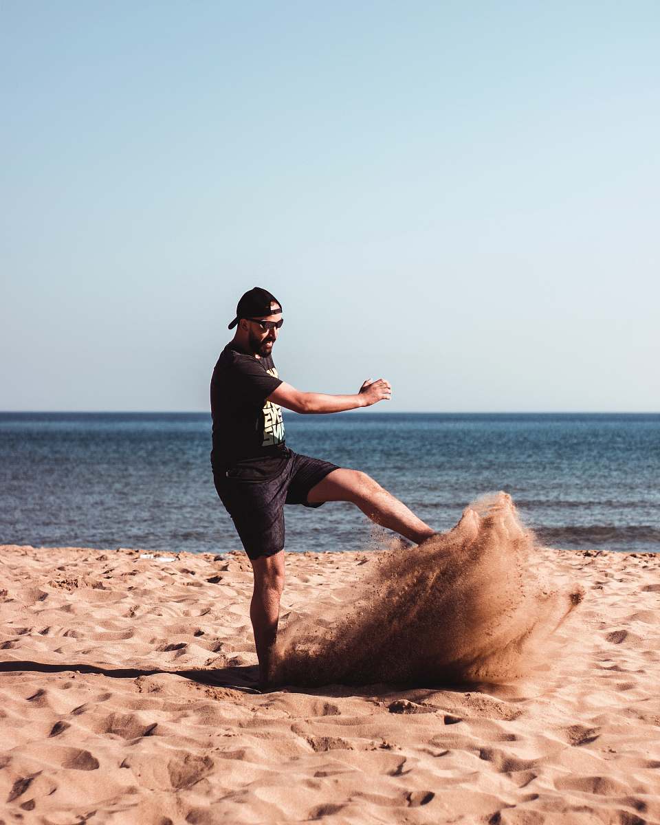 person man kicking a sand beside seashore during daytime nature