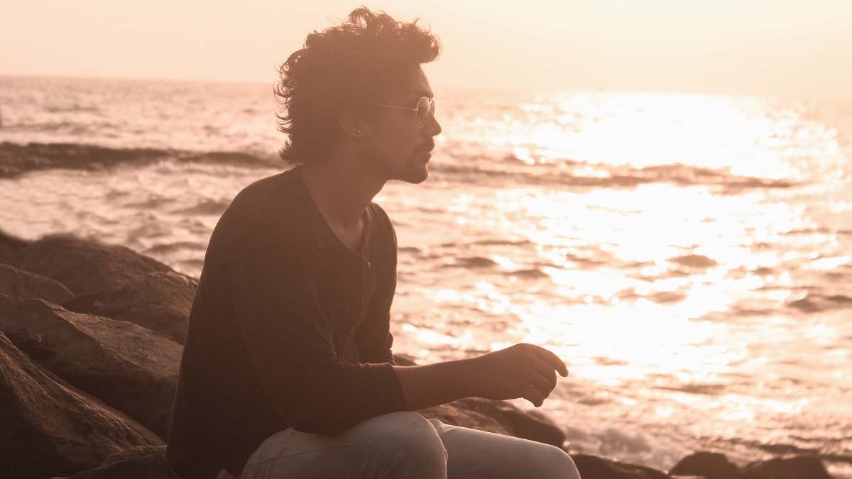 person man sitting on rock beside shore sitting