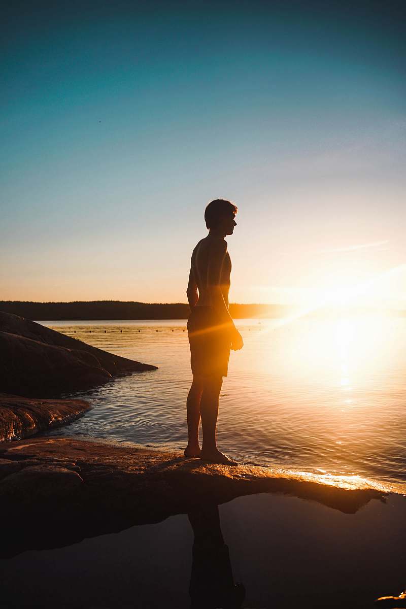 people man standing on rock besides body of water during sunset water