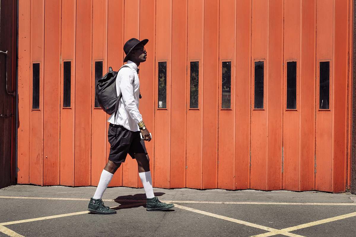 person man wearing black hat and white dress shirt walking on street near orange gate people
