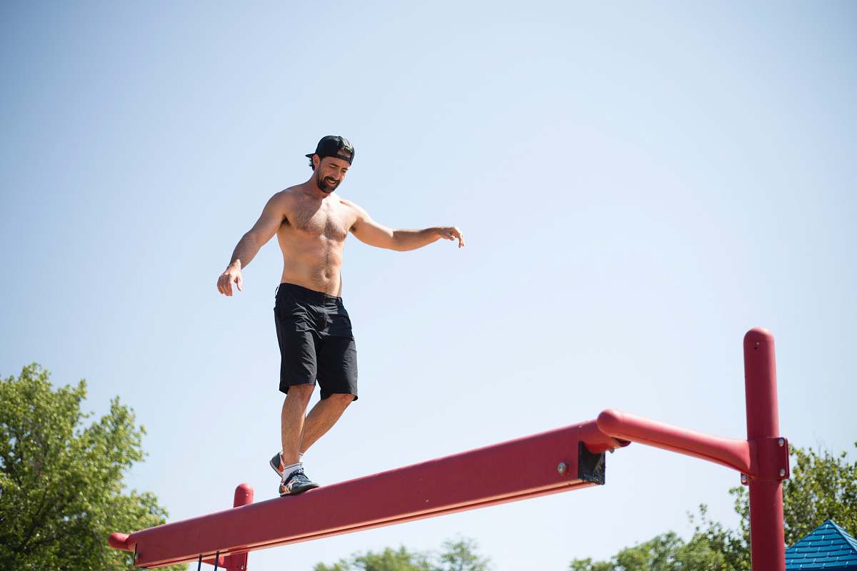 person man wearing black shorts walking on red metal beam people