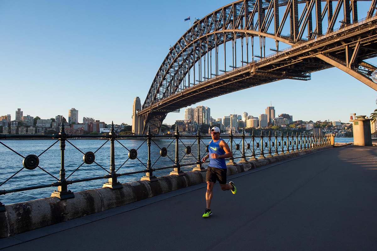 person man wearing blue tank top running under bridge building