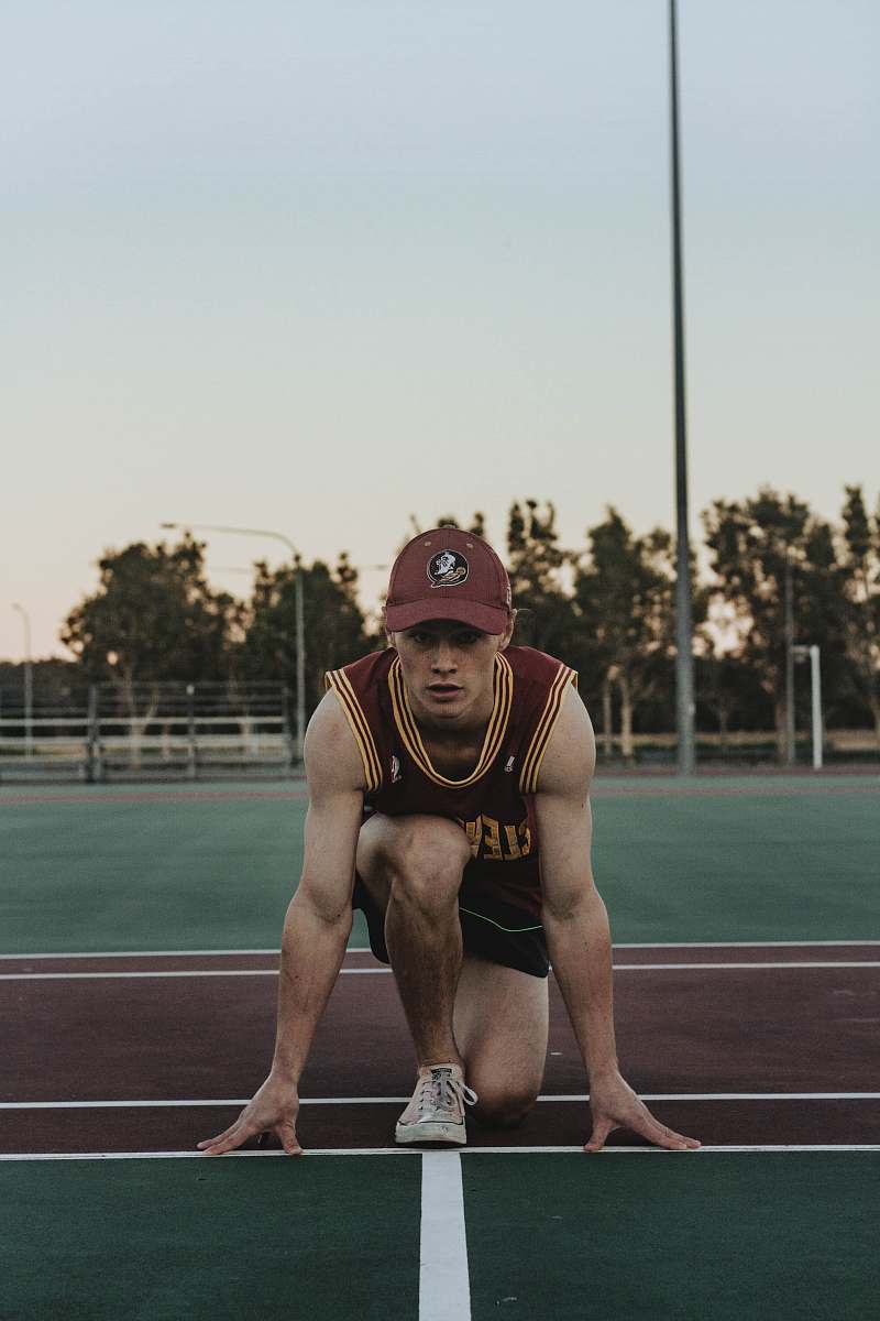 sports man wearing red and orange tank top preparing to run in ground during daytime sport