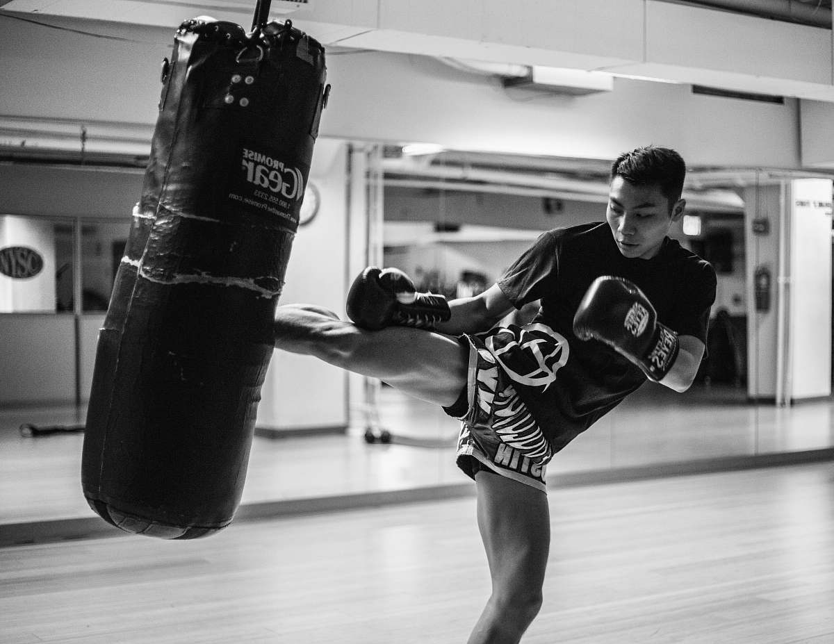 black-and-white man wearing training gloves kicking heavy bag inside gym near mirror walls boxing