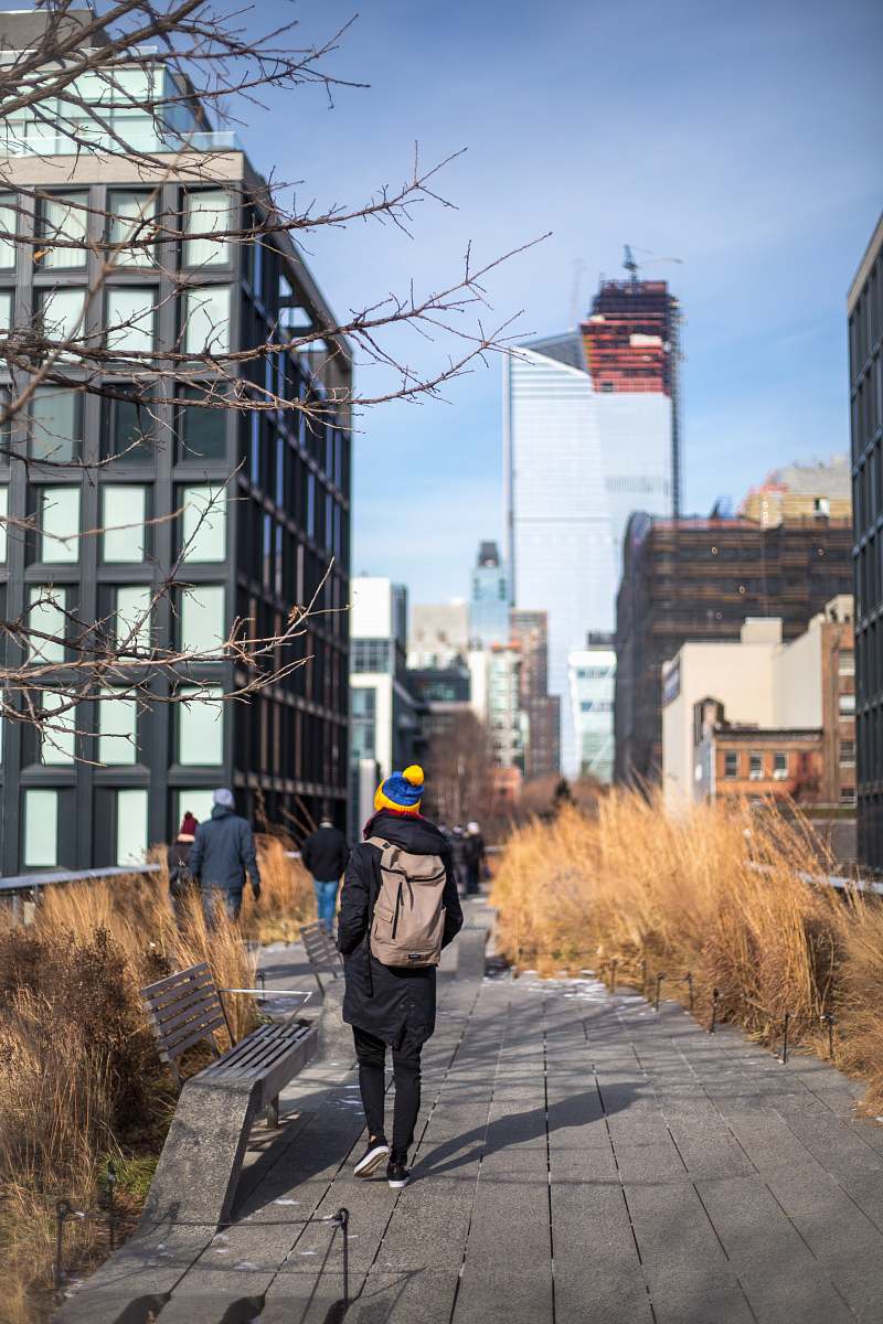 person person wearing winter clothes with brown backpack walking on gray pathway outdoors during day people
